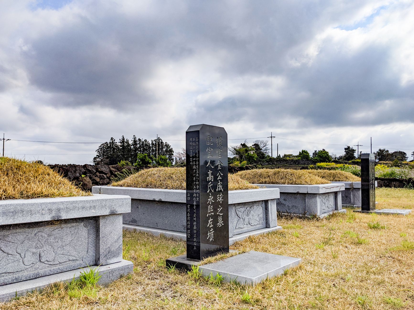 An outdoor scene of traditional Korean tombstones beneath a cloudy sky, evoking solemnity and heritage.