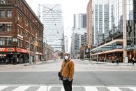在多伦多街道上，一个戴着口罩的人站在现代和历史建筑之间