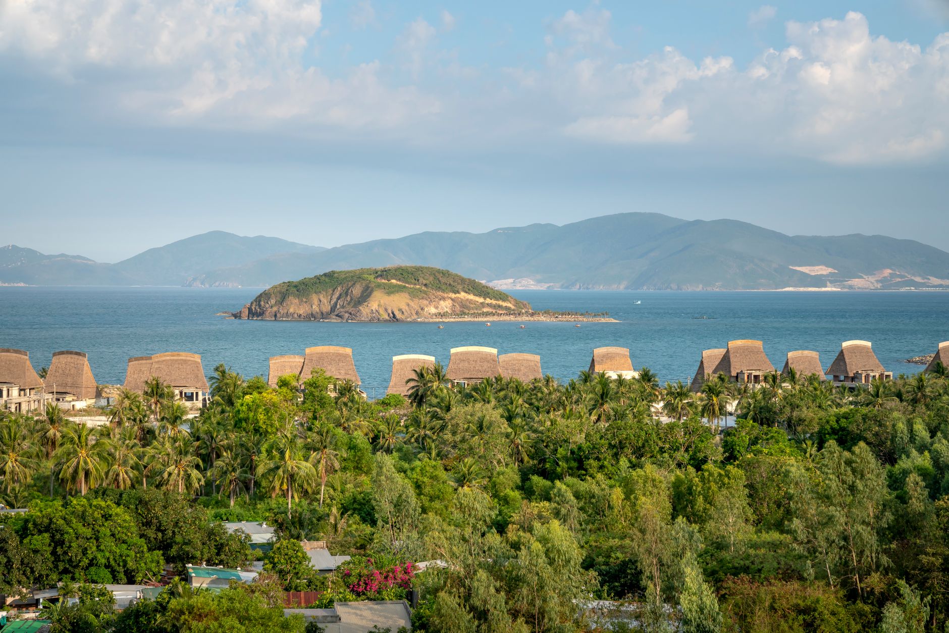 A picturesque view of a beachfront resort with an island and mountains in the background.