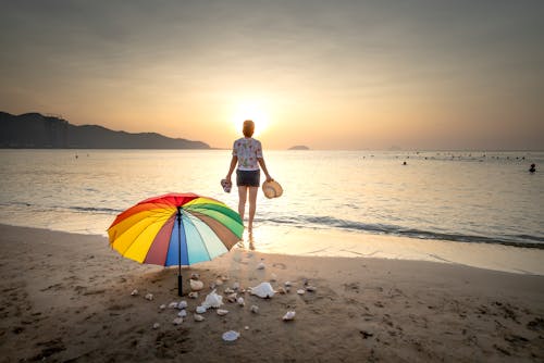 Free Woman Standing On The Seashore During Sunset Stock Photo