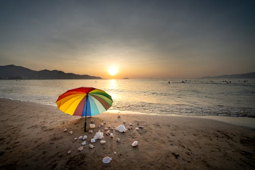 Free Red Yellow and Blue Umbrella on Beach during Sunset Stock Photo