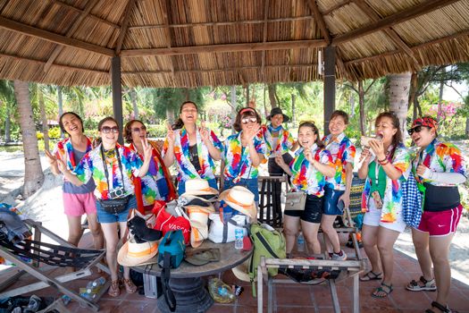Group of women enjoying a colorful and joyful gathering at a tropical beach hut under warm sunlight.