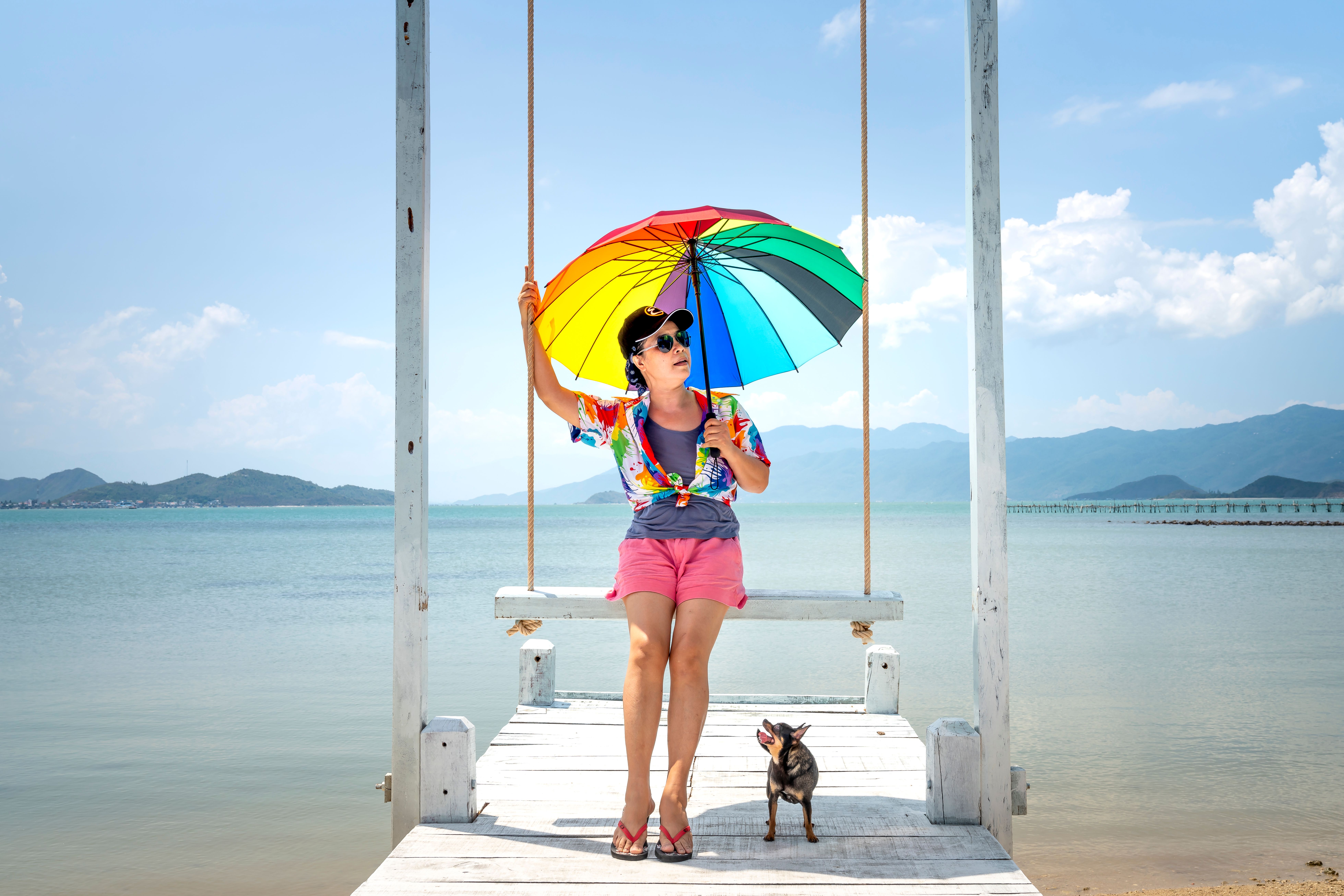 夏日，一名妇女和她的狗在海滩上充满活力的彩虹伞下荡秋千放松身心