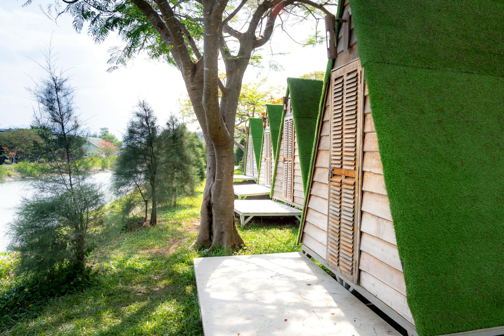 Picturesque scenery of green shore of river and wooden houses with triangular green roof located in row on sunny summer day