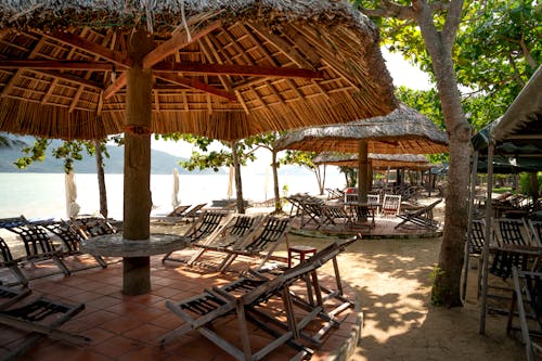 Brown Wooden Beach Lounge Chairs Under Nipa Hut