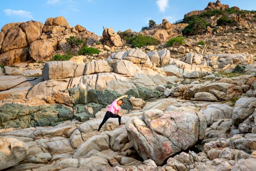 Free Woman in Pink Shirt and Black Pants Standing on Rocky Mountain Stock Photo