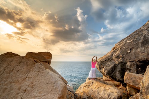 Woman in White Shirt Standing on Rock Formation Near Sea