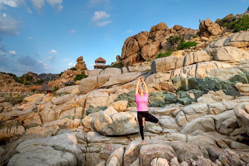 Woman in Pink Shirt and Black Pants Standing on Rocky Hill