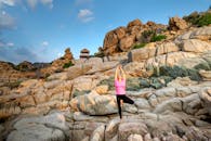 一名女子在晴朗的天空下，于岩石地形上摆出树姿势练习瑜伽