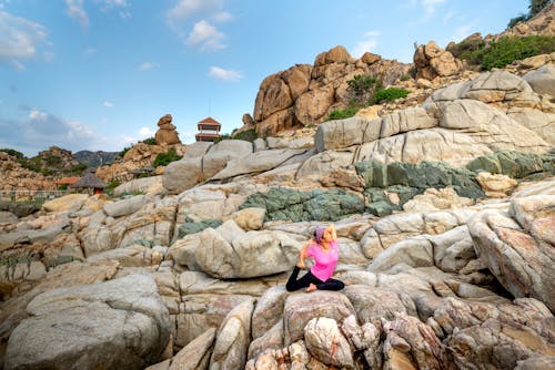 Woman in Pink Shirt and Black Pants Sitting on Brown Rock Formation