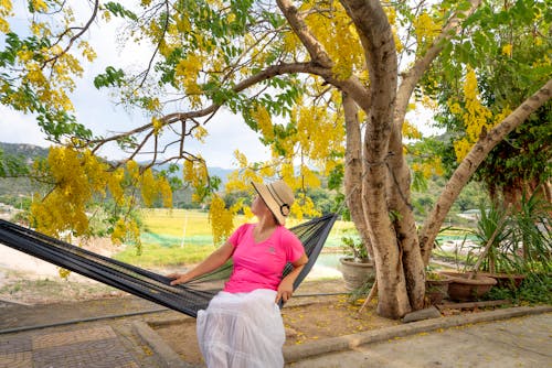 Woman in Pink Shirt and White Skirt Sitting on Black Hammock