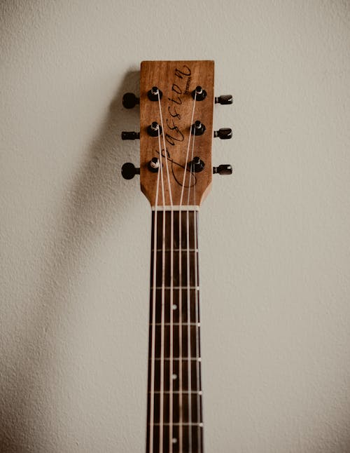 Free Brown Acoustic Guitar Leaning on White Wall Stock Photo