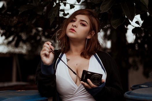 Stylish woman posing with a camera in a natural outdoor setting.
