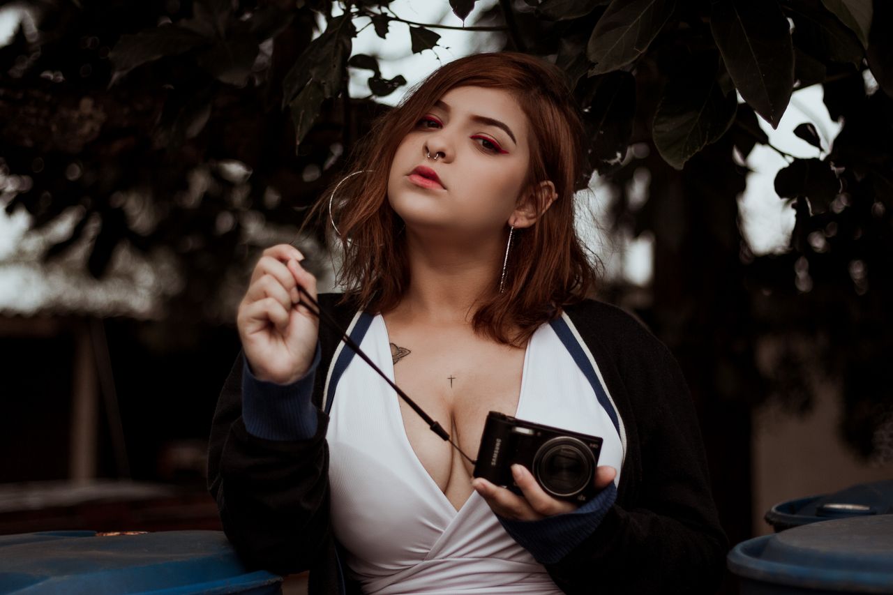 stylish woman posing with a camera in a natural outdoor setting
