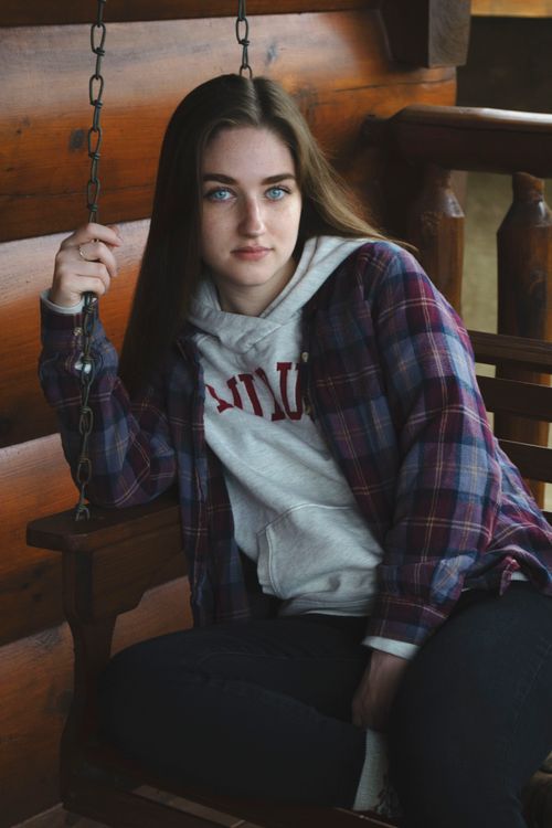 Free Young woman in casual wear sitting on a wooden swing inside a cozy room. Stock Photo