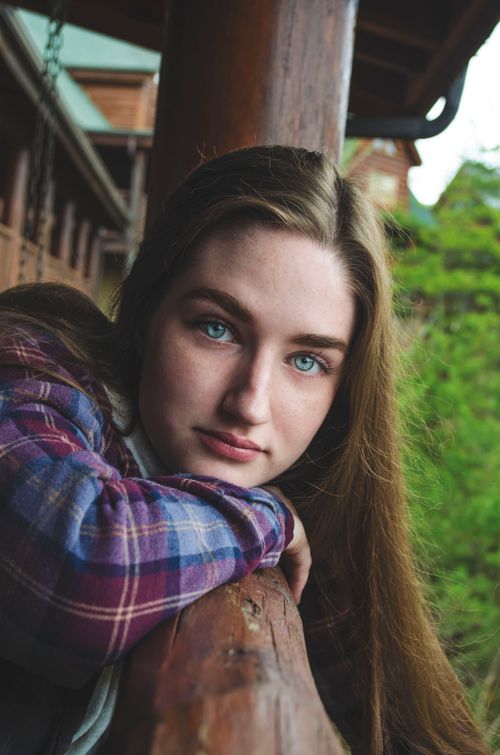 Free Teen girl with long hair leans on a wooden railing outdoors, in a contemplative pose. Stock Photo