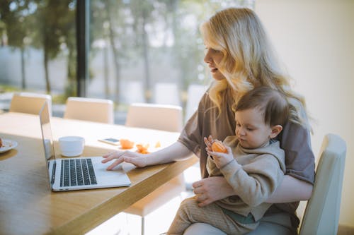 Free Woman Carrying her Baby and Working on a Laptop Stock Photo