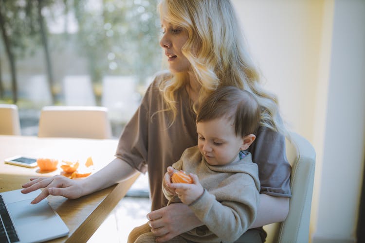 Photo Of Woman Carrying Her Baby While Working On Her Laptop