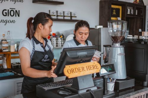 Free Two baristas work at a coffee shop counter with a cash register and equipment. Stock Photo
