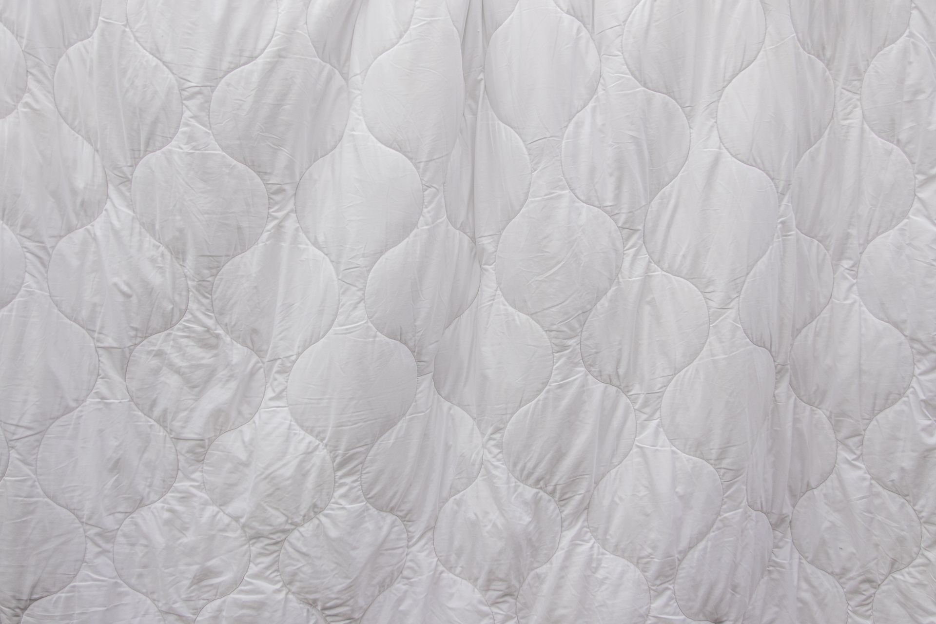 Close-up of a white quilted textile, showcasing an elegant pattern ideal for home decor and bedding.