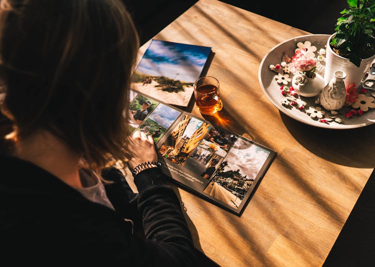 Overhead Shot Of Woman In Black Long Sleeves Looking At Photographs On A Magazine 