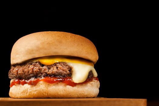 Delicious cheeseburger with melted cheese and ketchup on a wooden table.
