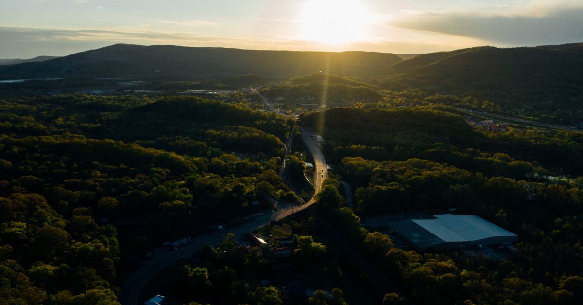 Drone shot of a sunlit road winding through lush forest and hills near Chattanooga, Tennessee.