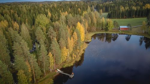 Free Scenic aerial view of a lake and autumn forest in Finland featuring colorful foliage and a red cabin. Stock Photo
