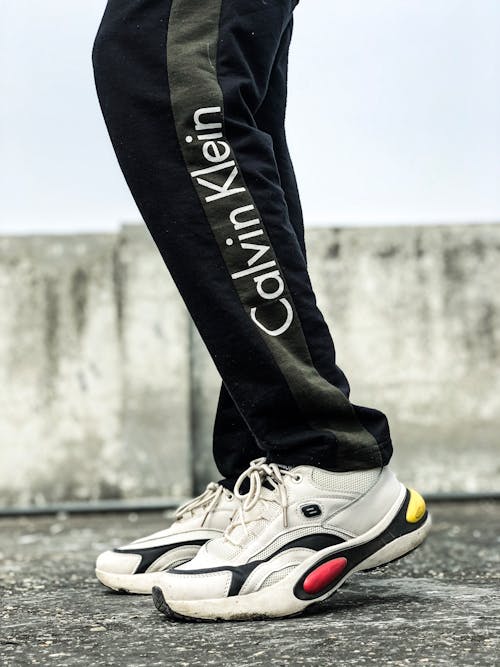 Side view of crop unrecognizable person standing on asphalt road in stylish sneakers and activewear