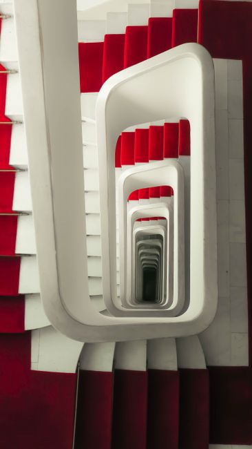 A striking modern staircase with red accents spirals downward in a contemporary design.