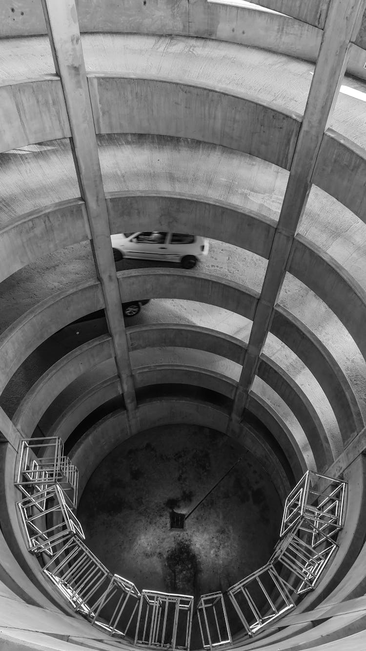 Grayscale Photo Of A Car On A Spiral Ramp On Multi Level Parking Area
