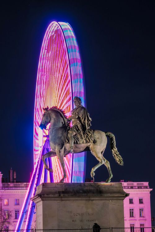 Free Night view of a historic equestrian statue with a vibrant illuminated ferris wheel in Lyon, France. Stock Photo
