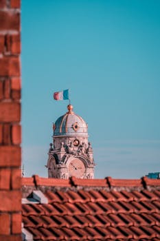 A clock tower topped with the French flag surrounded by city rooftops against a clear blue sky.