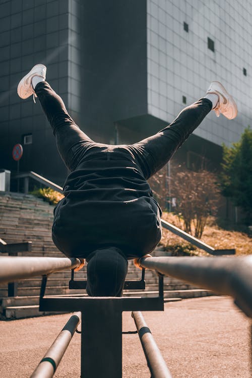 Back view of anonymous young male athlete in activewear doing trick on metal railings  while training in outdoor sports ground in modern city on sunny day