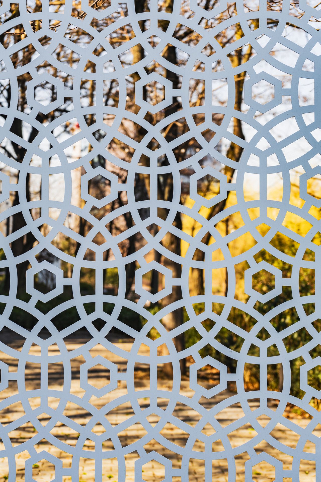 White laser-cut fence panels with a geometric pattern in an autumn park