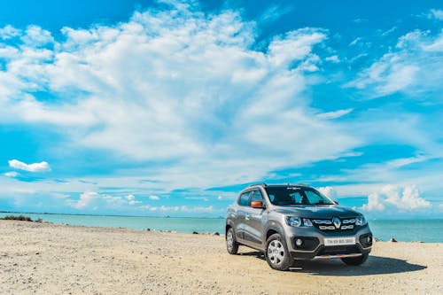 Stylish modern SUV car parked on sandy shore near endless sea against bright blue sky on sunny day