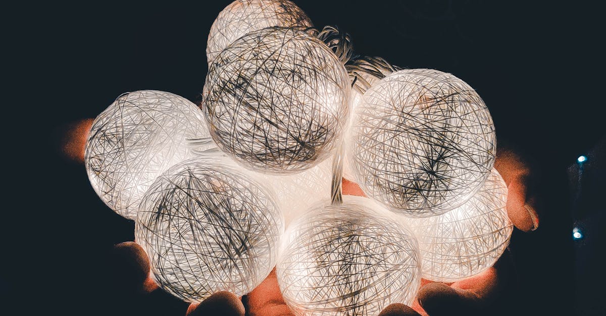 Illuminated Christmas balls with LED lights in hands of anonymous person in dark room during holiday preparation