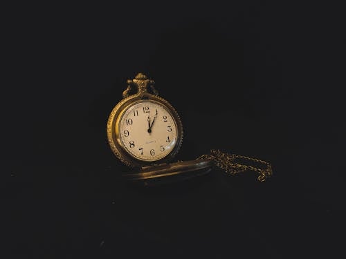 Vintage watch with chain and white dial placed on black background in studio