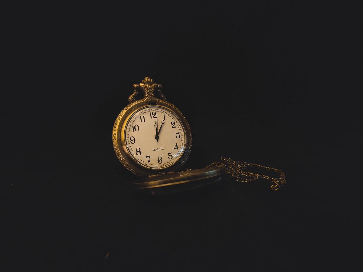 A worn gold pocket watch and chain lit against a black background — photo by Fredrick Eankels on Pexels