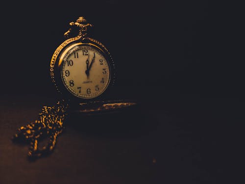 Round vintage chromed clock with decor and chain placed on black background in studio