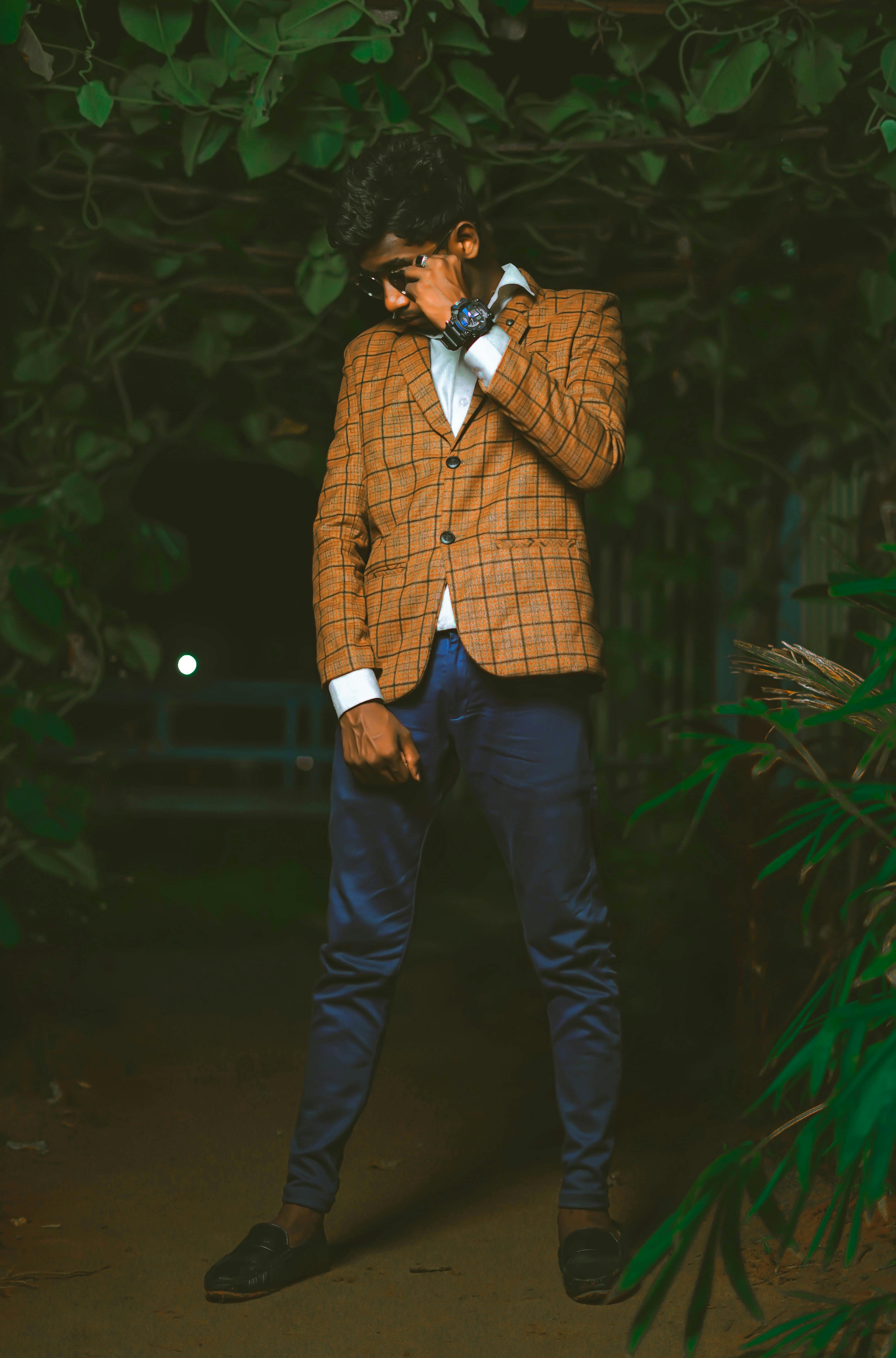 A young man in a checkered blazer poses confidently outdoors at night.