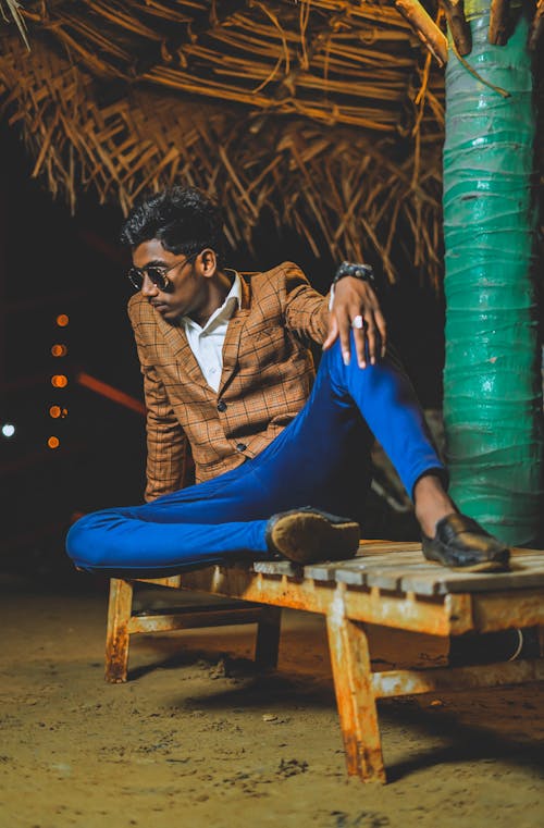 Indian man in trendy clothes sitting under palm