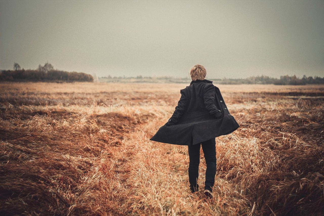a person walks alone in a scenic autumn field wearing a coat