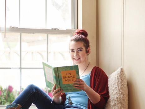 Smiling woman enjoying a leisure reading moment indoors by the window.. smiling, woman, enjoying