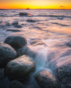 Capture the serene beauty of a sunset illuminating a rocky seashore in Porvoo, Finland.