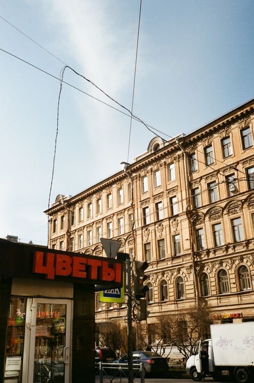 Free Low angle of historic stone house facade near city road and driving vehicles passing by flower shop under serene sky and wires in daylight in Russia Stock Photo