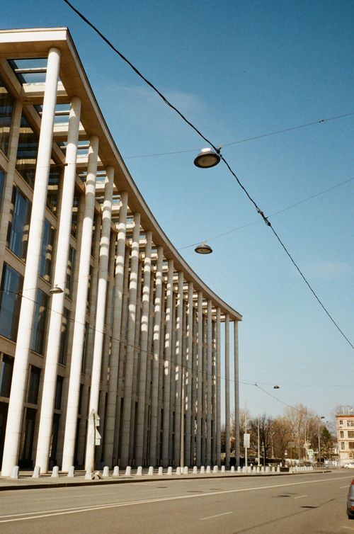 Free Aged house exterior with stone colonnade near asphalt roadway with marking lines under wire with street lamps and blue cloudy sky in town Stock Photo