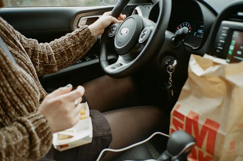 Person in Brown Long Sleeve Shirt Driving and Eating