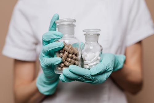 Person Holding Clear Glass Jar With Brown and White Medicines