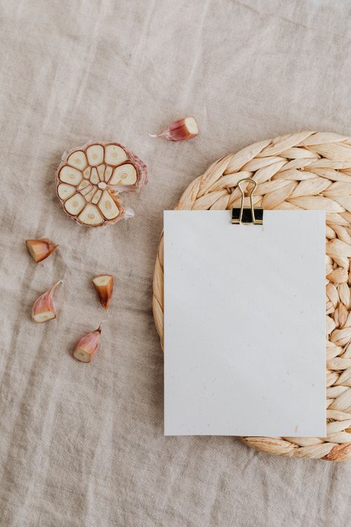 Free A top-down view of garlic cloves and a blank paper on a woven mat, perfect for food photography. Stock Photo